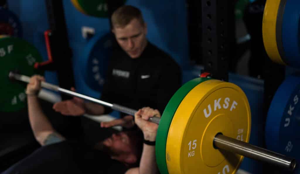 Man Bench pressing with personal trainer helping