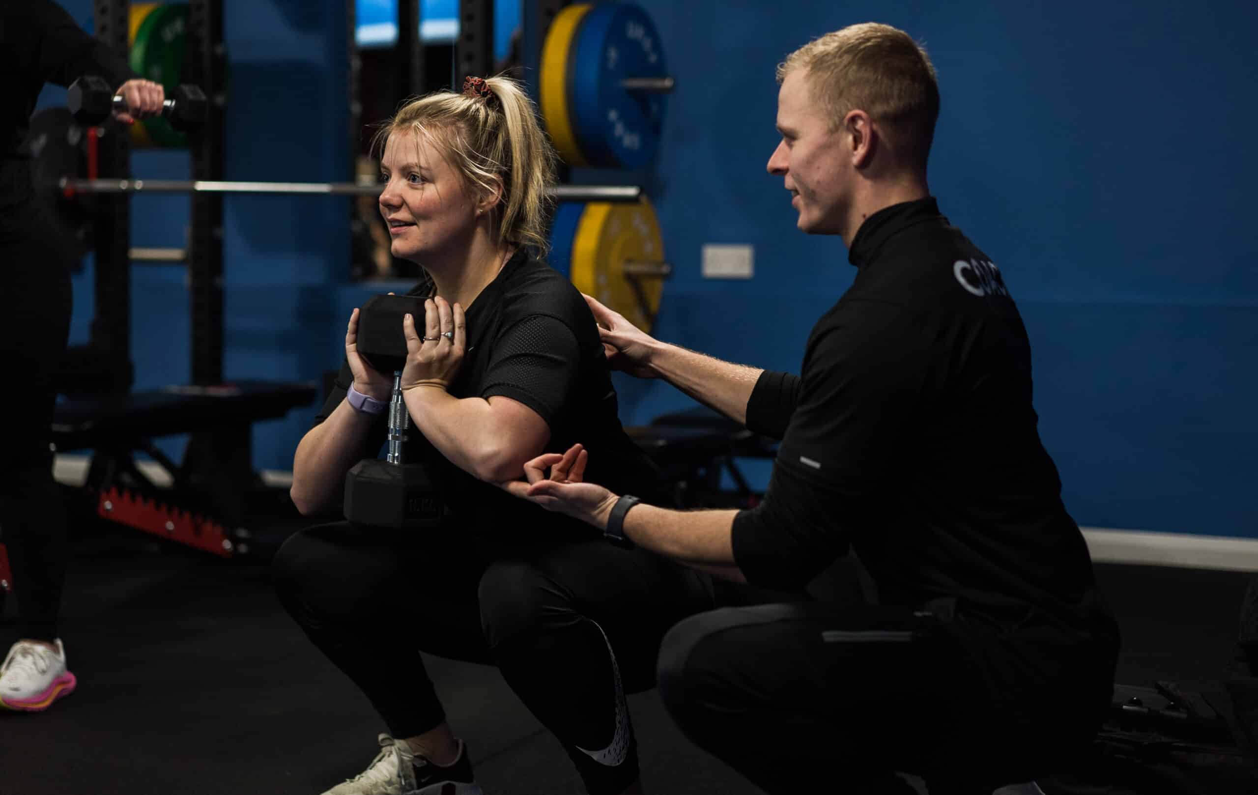 Man helping woman squat with dumbbell